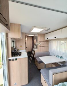 Wnętrze przyczepy Adria Aviva 522 PT – kuchnia z czajnikiem, stół jadalniany i dostęp do łóżek piętrowych