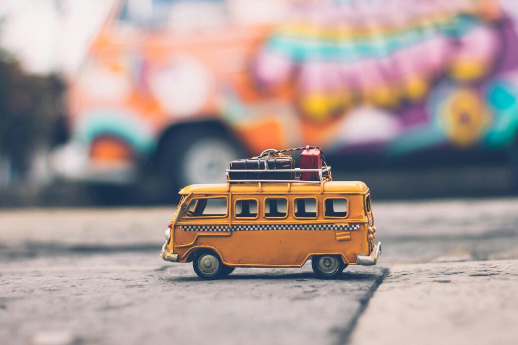 Zabawka w kształcie żółtego busa z bagażem na dachu na tle rozmytego obrazu – kreatywna grafika ilustrująca kontakt z wypożyczalnią Tru Camp